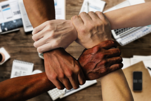 Four linked hands above desktop.