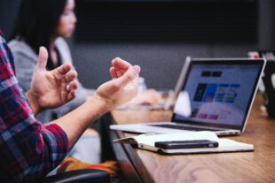 Man sitting in front of laptop explaining ideas using hand gestures.